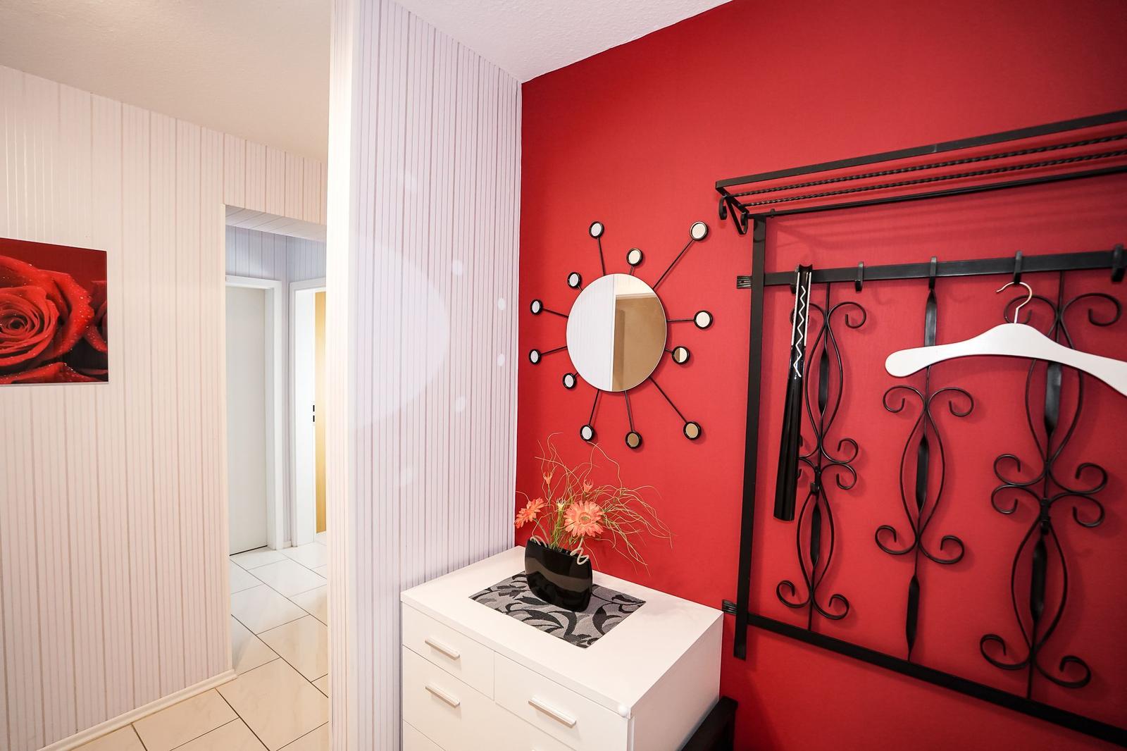 Schlafzimmer mit roter Wand, Spiegelschmuck und Garderobe.