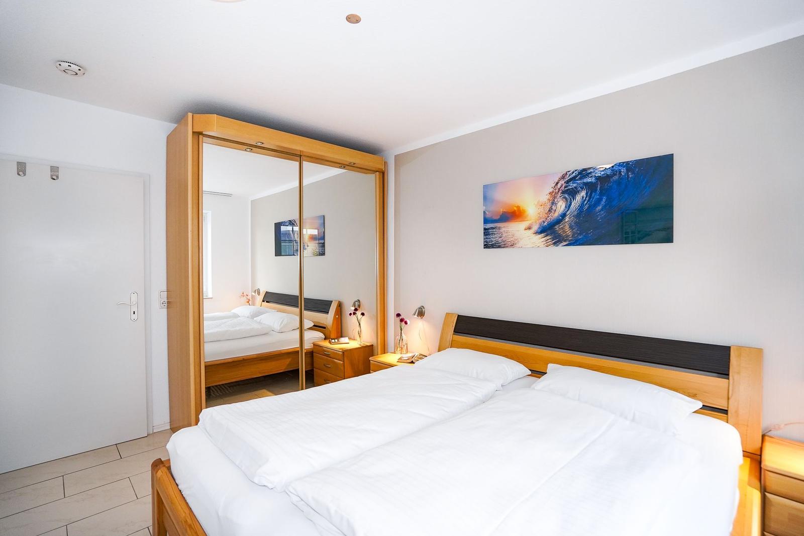 Schlafzimmer mit Doppelbett, Kleiderschrank und Wandbild.