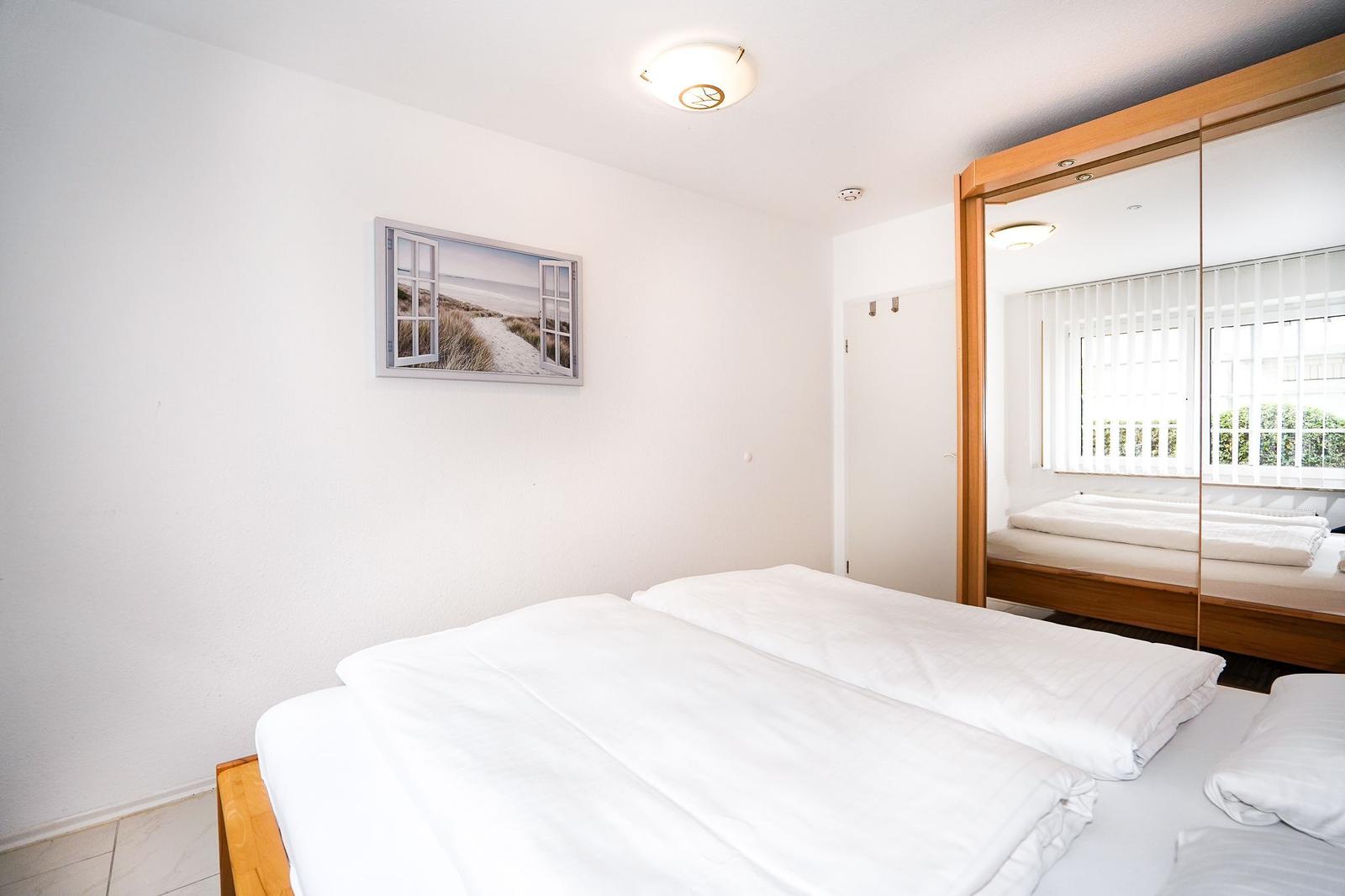 Schlafzimmer mit Doppelbett, Spiegelschrank und Wandbild.