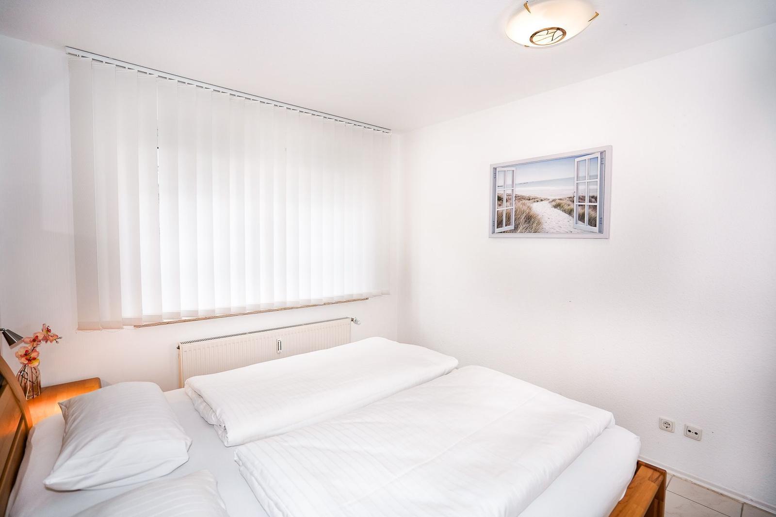 Schlafzimmer mit Doppelbett, Fenster mit Jalousie und Wandbild.