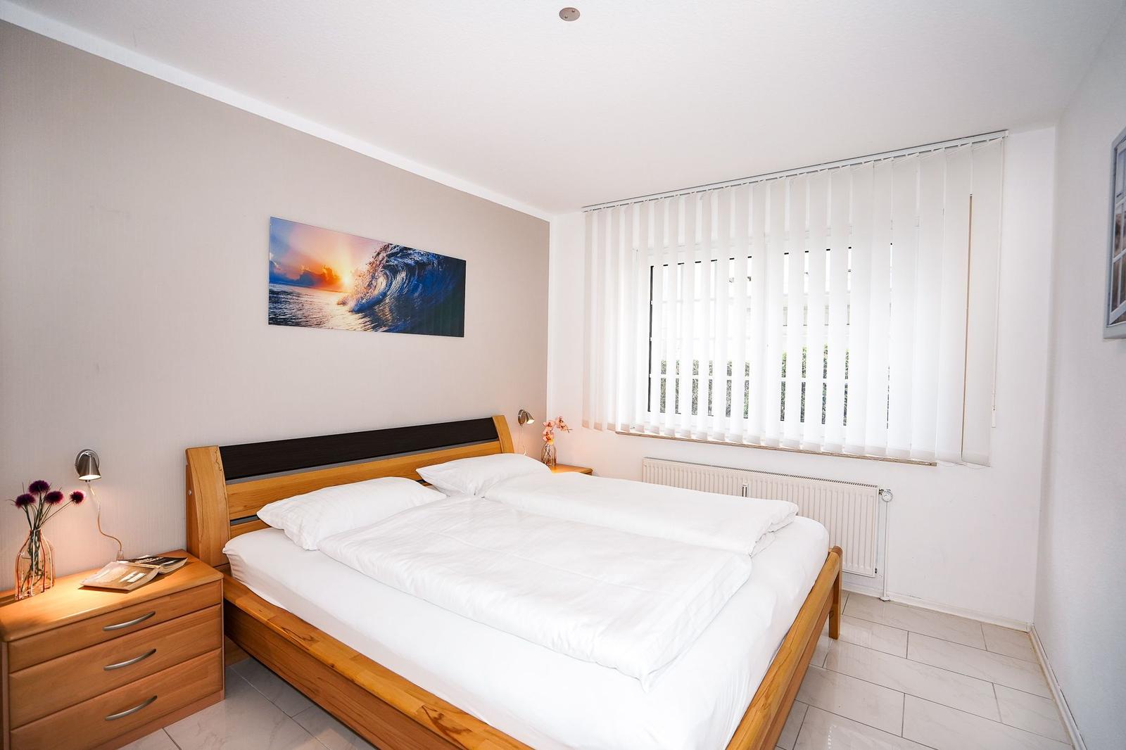 Schlafzimmer mit Doppelbett, Nachttischen und Fenster mit Jalousie.