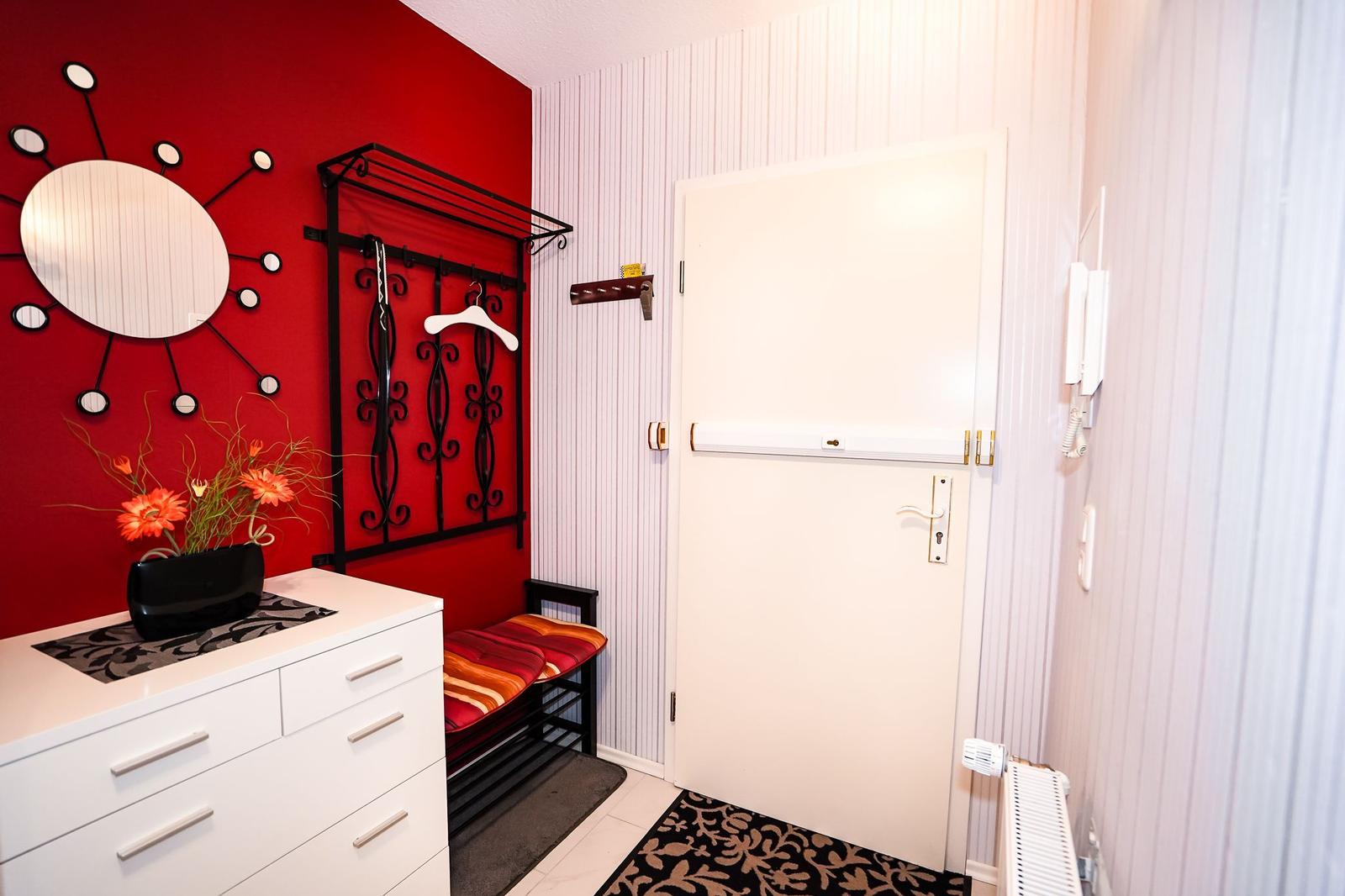 Eingangsbereich mit roter Wand, Garderobe und weiße Tür.