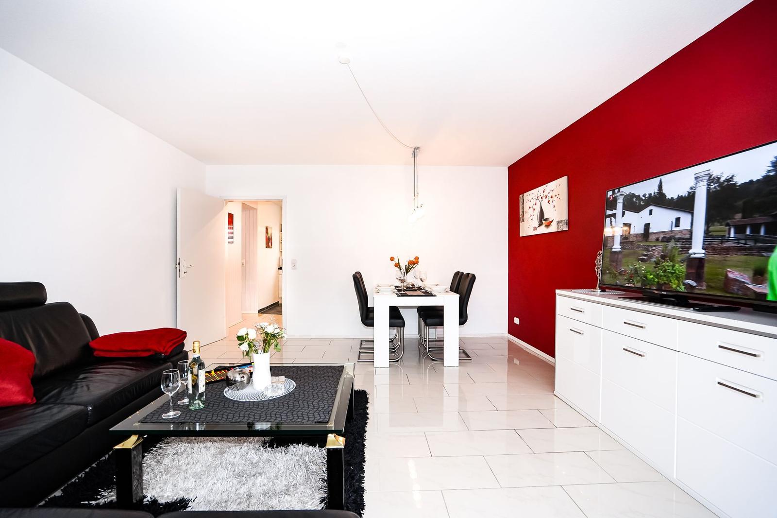 Wohn- und Essbereich mit roter Wand, Sofa, Esstisch und Fernseher.