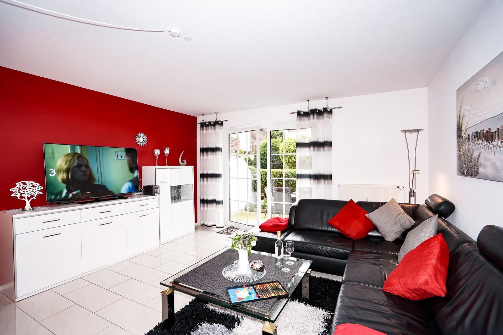 Wohnzimmer mit schwarzer Ledercouch, roter Wand und Glas-Tisch.