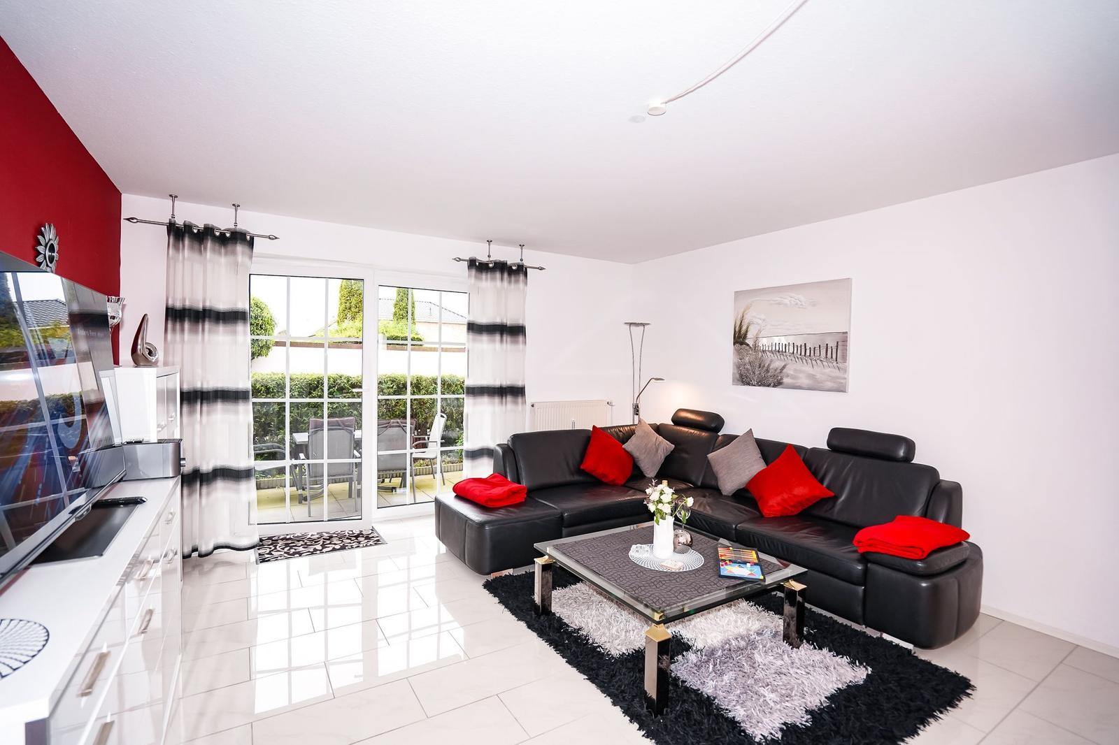 Wohnzimmer mit schwarzer Ledercouch, Glas-Tisch und Terrasse.