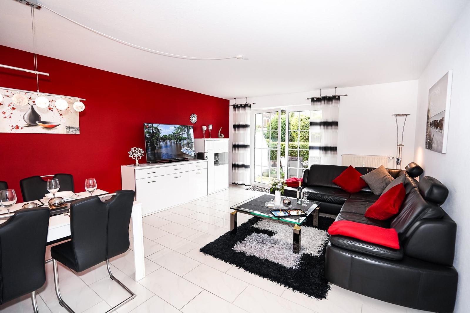Wohn- und Essbereich mit roter Wand, schwarzen Ledersofas und Glas-Tisch.