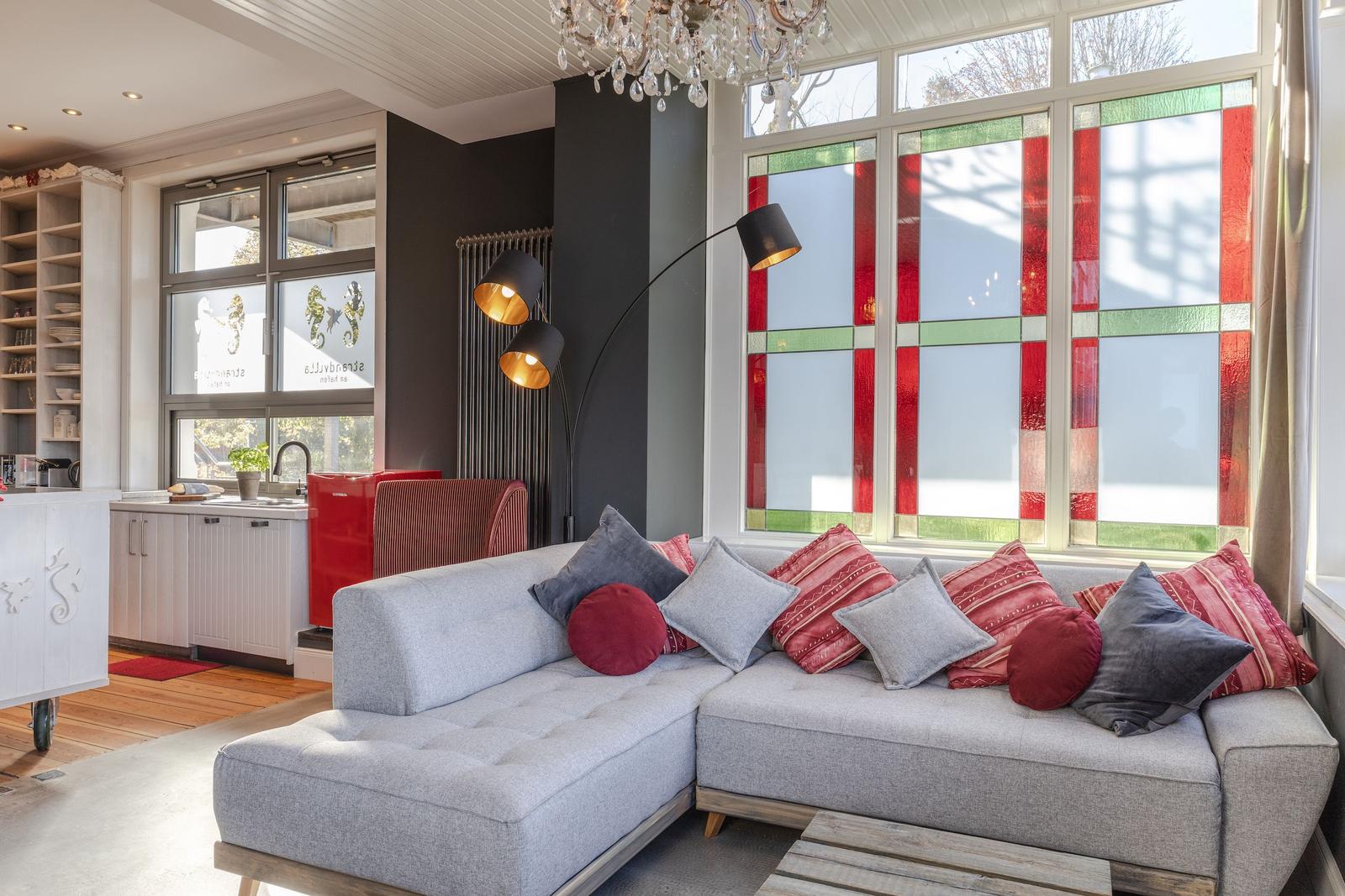 Ein Wohnzimmer mit grauem Sofa, bunten Kissen und farbigen Fenstern.