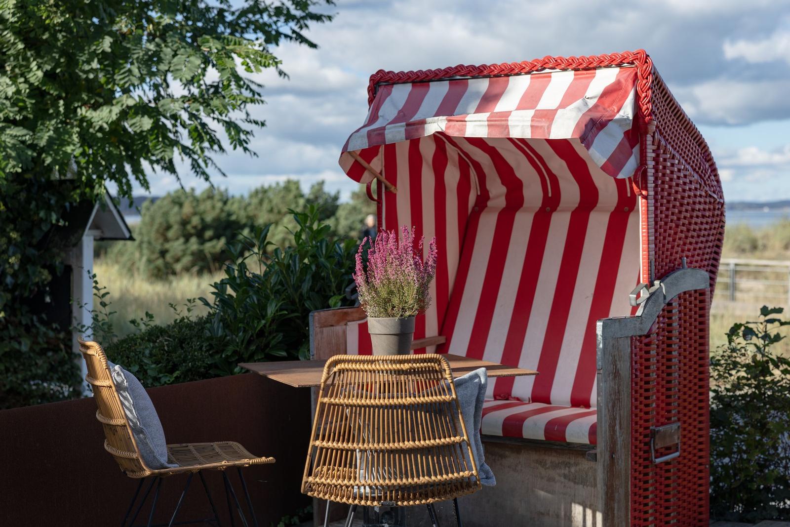 Rote Strandkörbe mit Streifen, Tisch und Stühle auf Terrasse mit Blick auf Grün und Wasser.