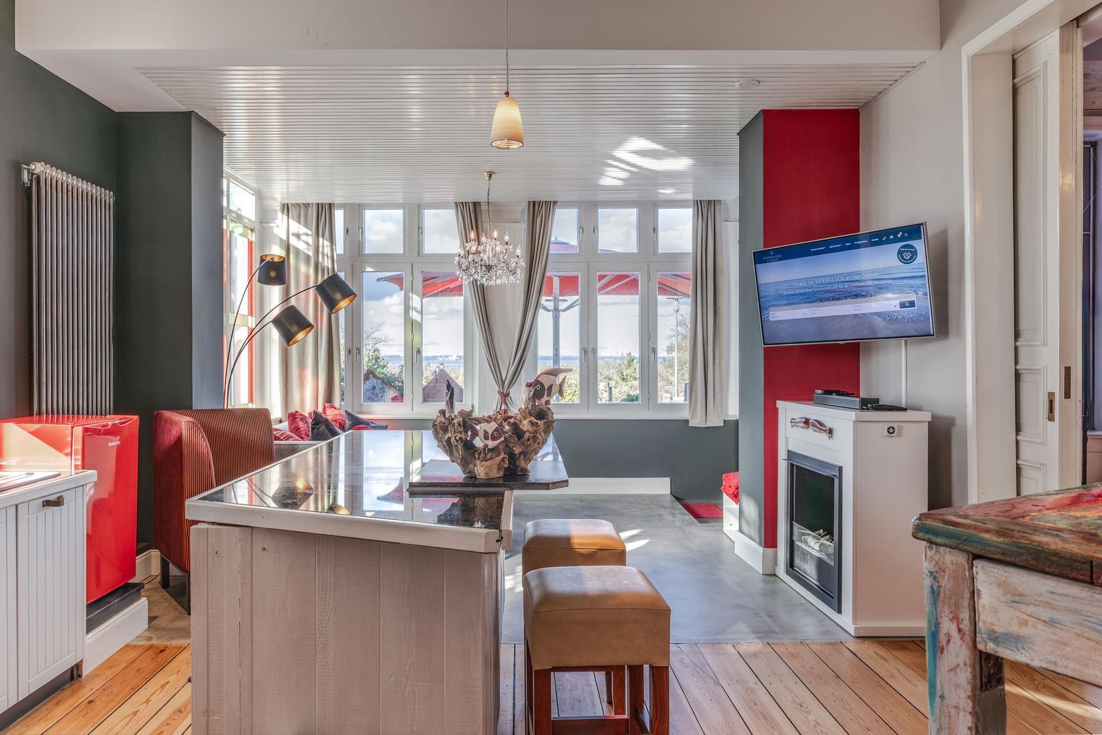 Wohnbereich mit Kücheninsel, Fernseher und Blick auf den See.