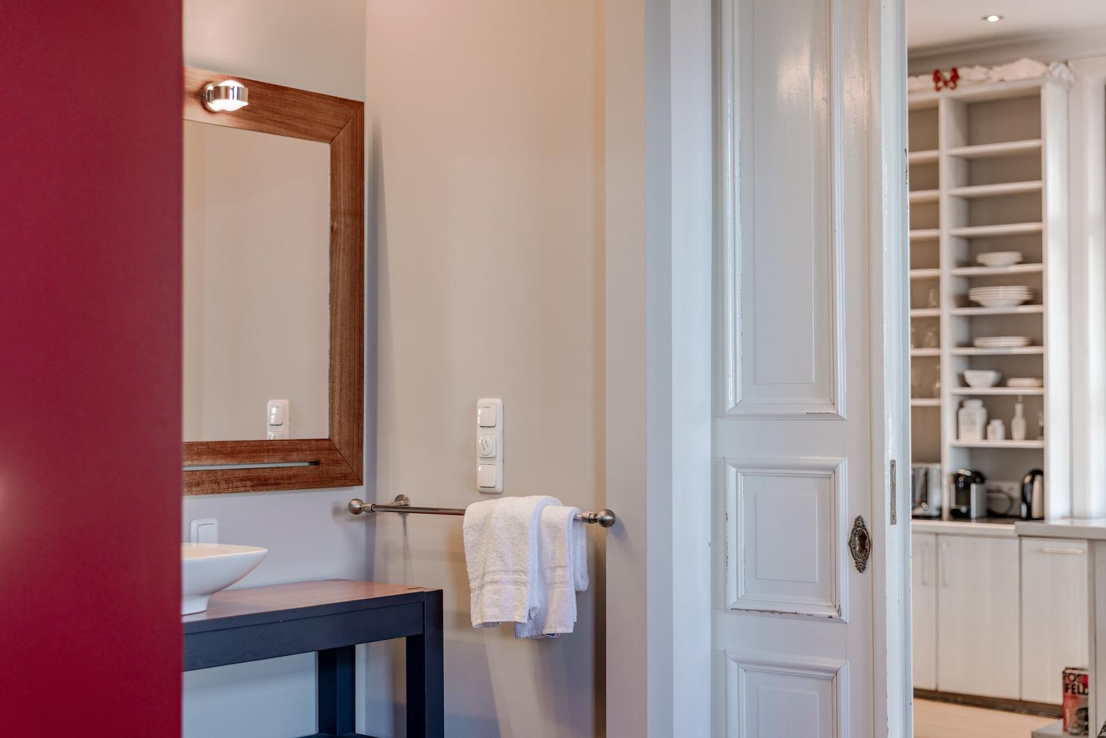 Badezimmer mit Spiegel und Handtuchhalter. Durchgang zur Küche mit Schränken.