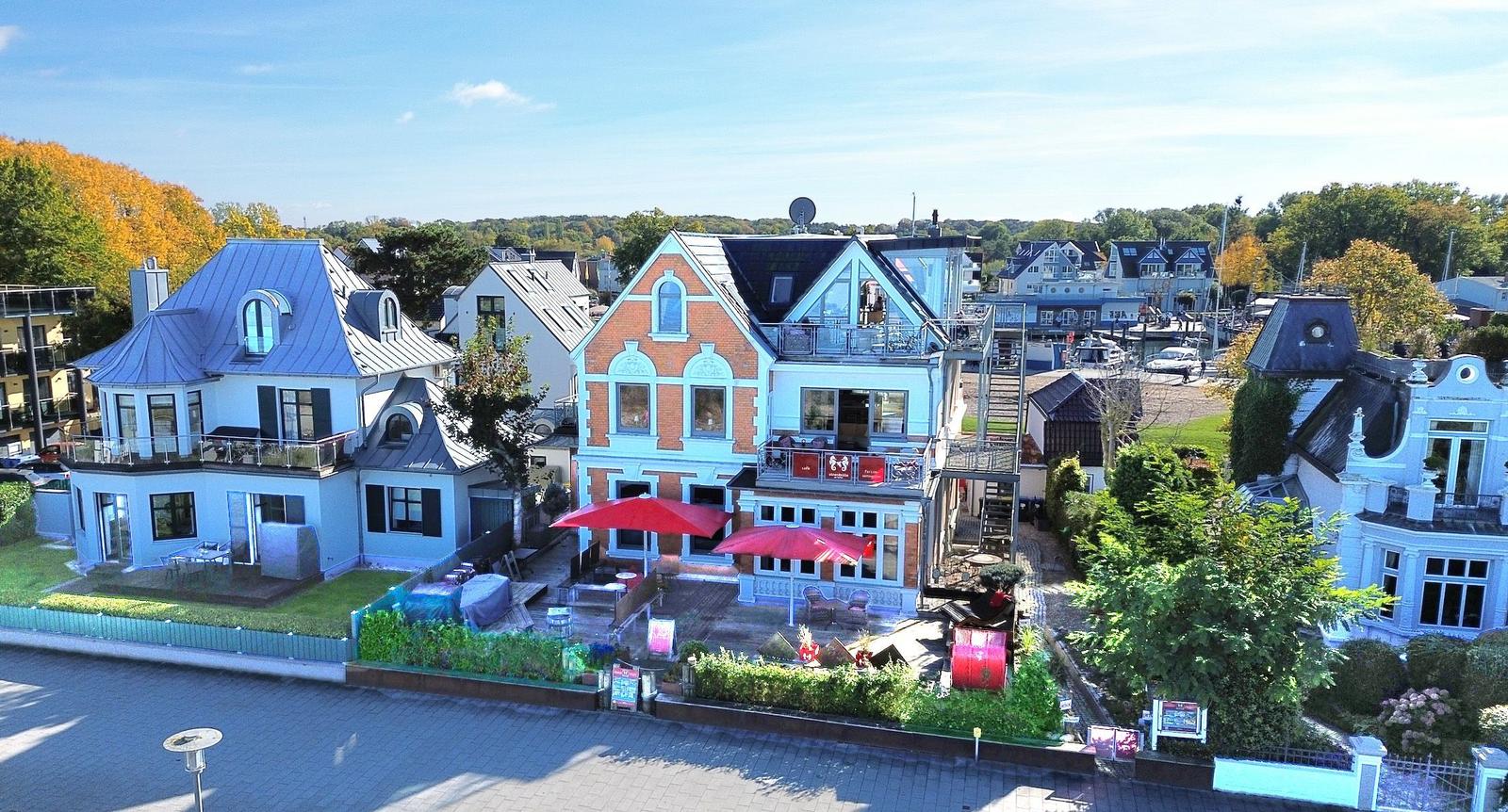 Haus mit Terrasse und roten Sonnenschirmen. Hinterhof mit Garten und Bäumen.