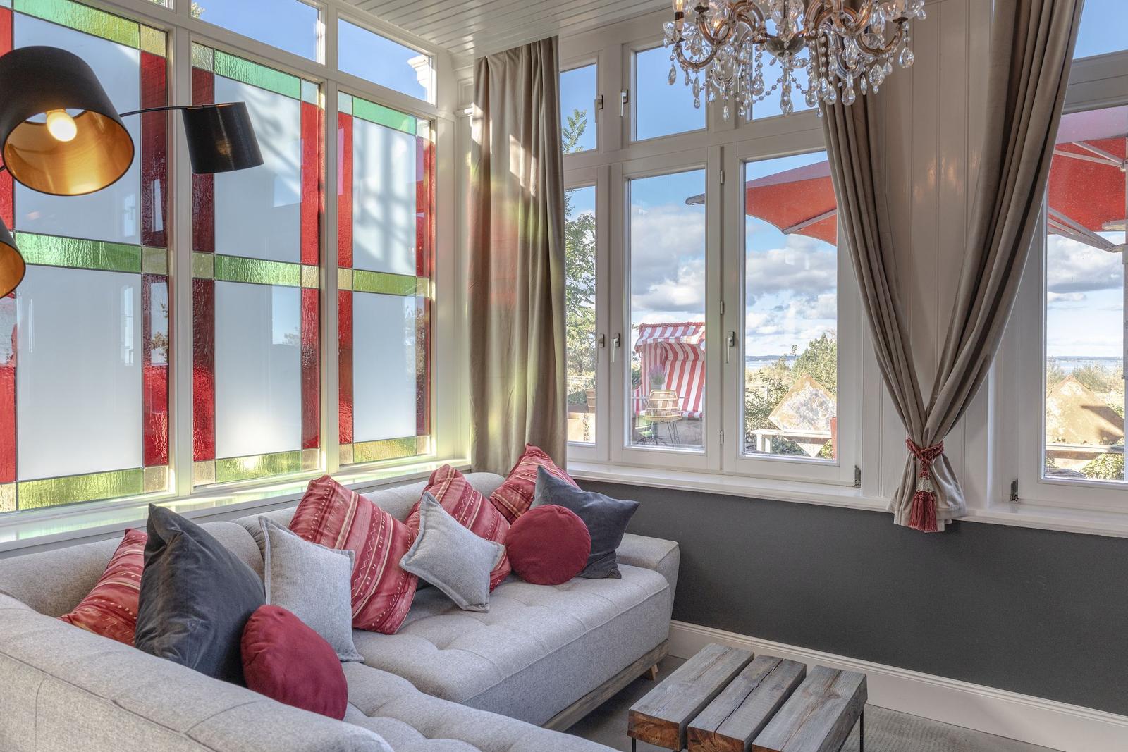 Ein Wohnzimmer mit Sofa, Kissen und Fenstern mit bunten Glasflächen.