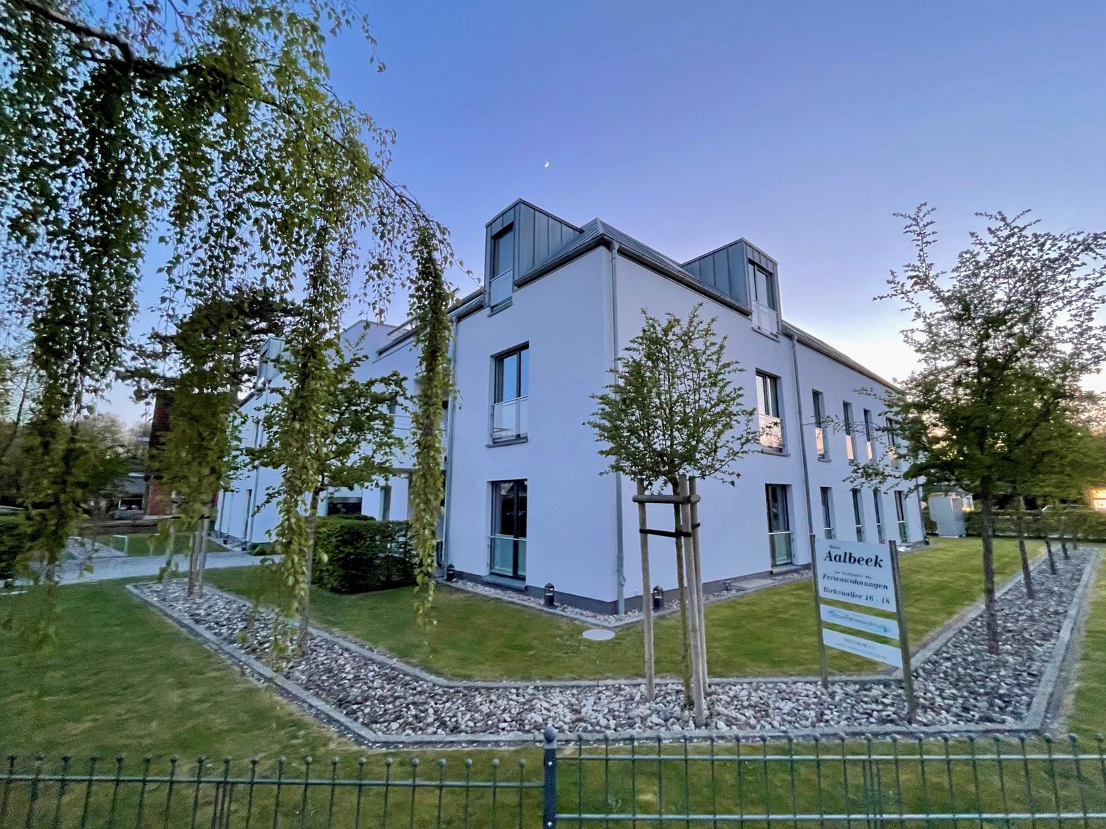 Moderne Ferienwohnungsanlage mit Grünanlagen und Schild.
