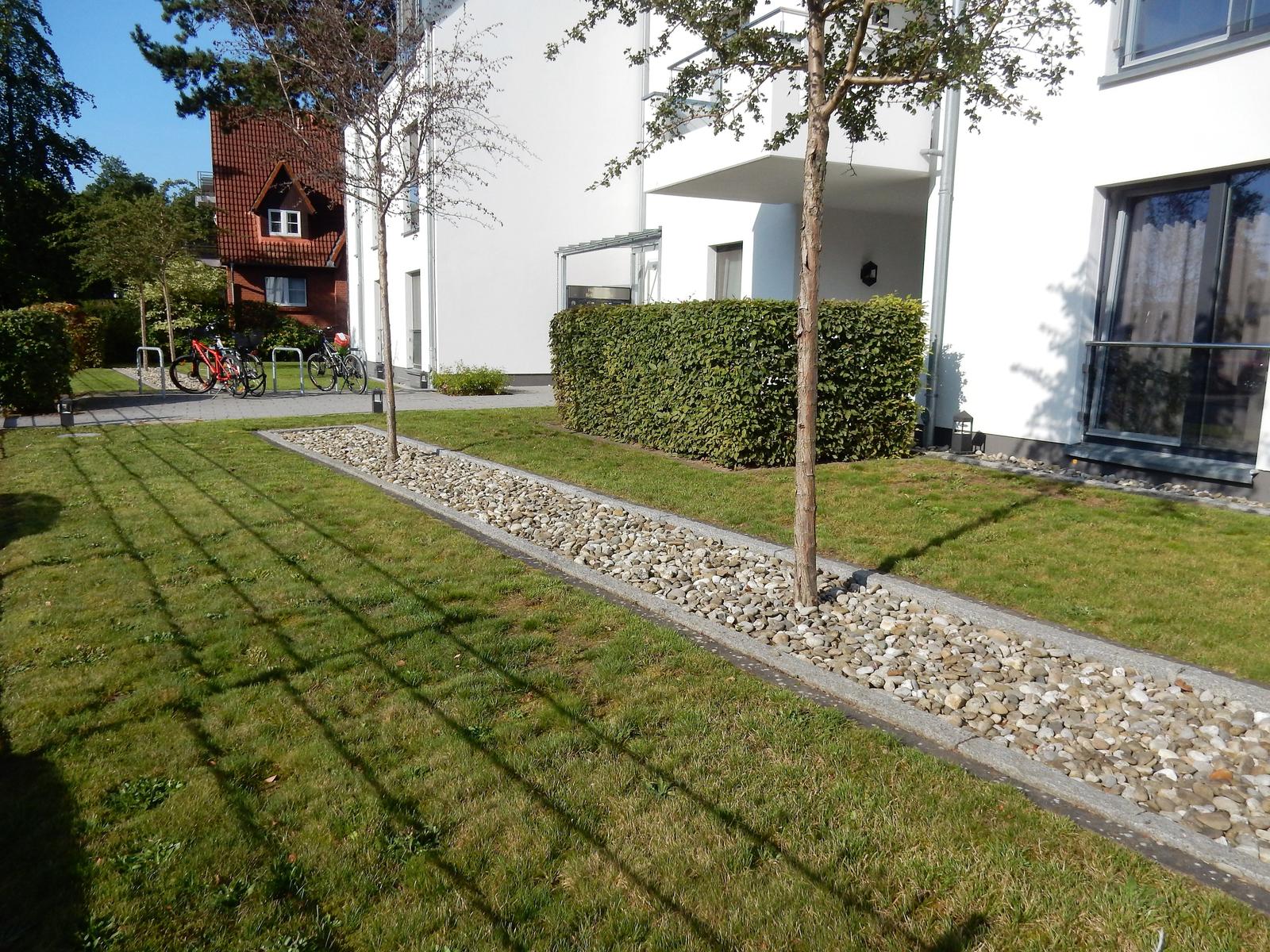 Garten mit Rasen, Kiesbeeten und Bäumen vor modernen Wohnhäusern.