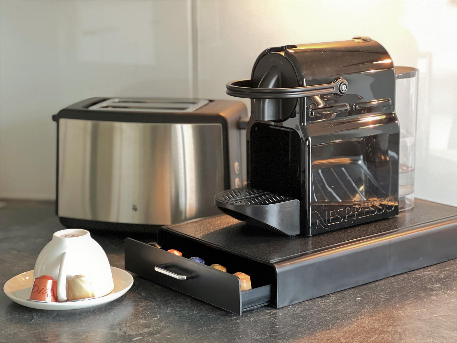 Kaffeemaschine und Toaster auf Küchenarbeitsplatte mit Kapseln und Tasse.