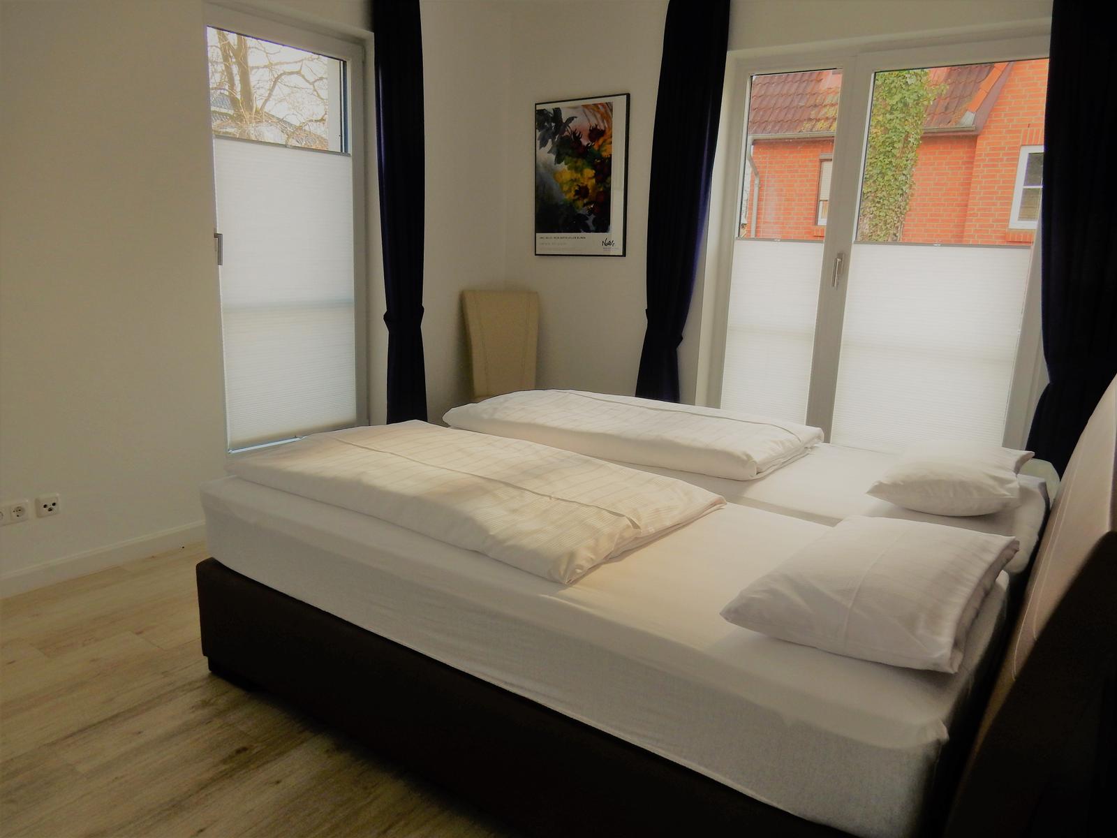 Schlafzimmer mit Doppelbett, Fenstern und Wandbild.