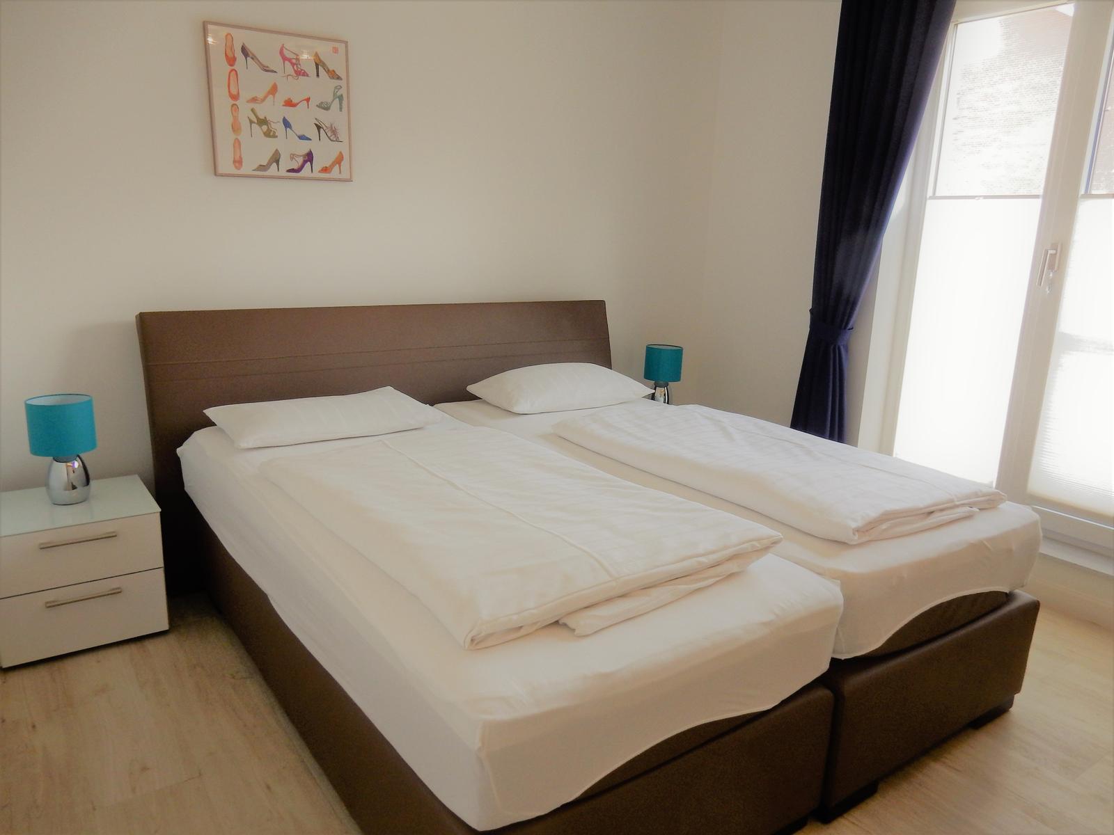 Schlafzimmer mit Doppelbett, zwei Nachttischen und Fenster mit Vorhängen.