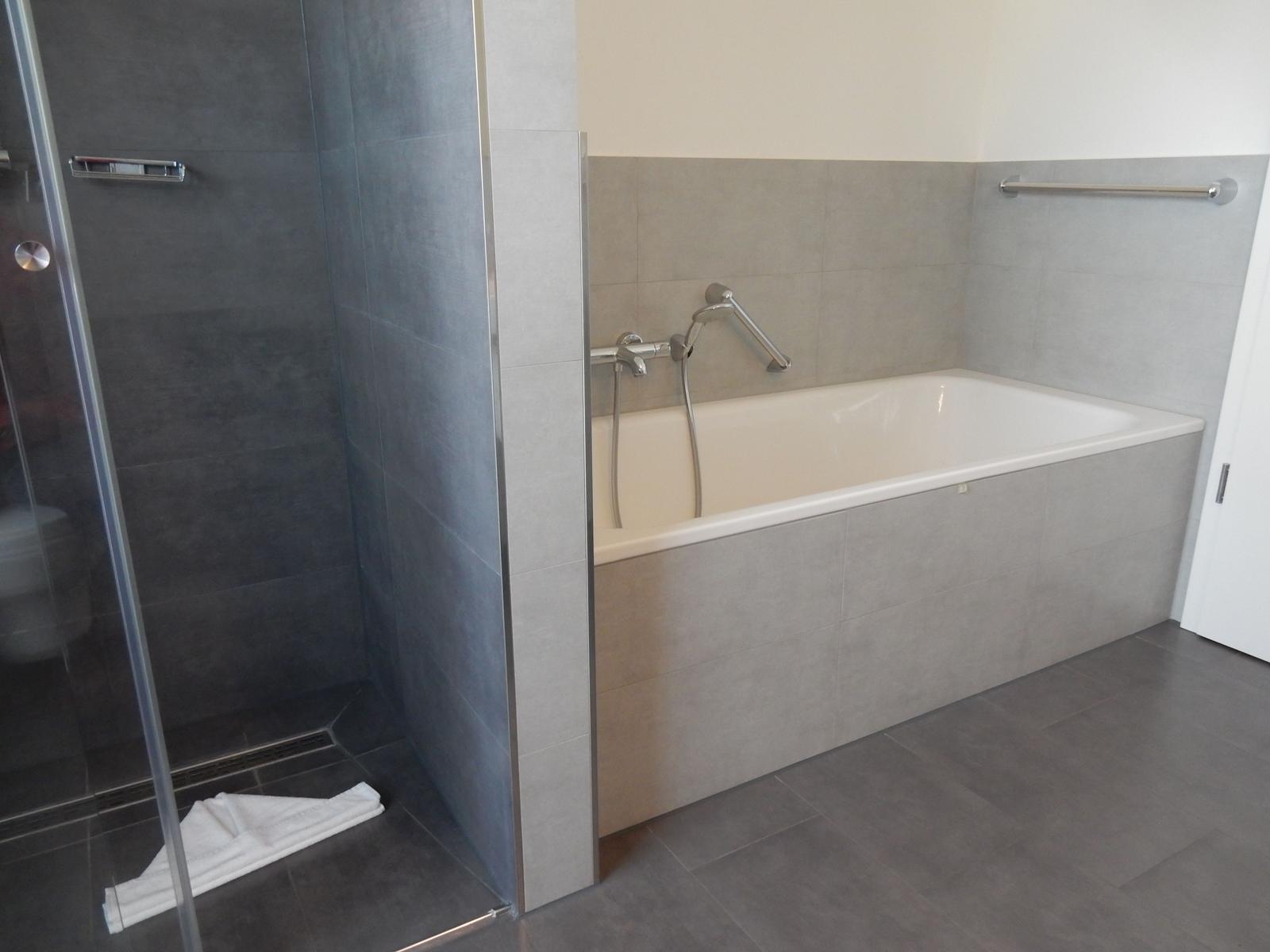 Bad mit Dusche und Badewanne, graue Fliesen und Chromarmaturen.