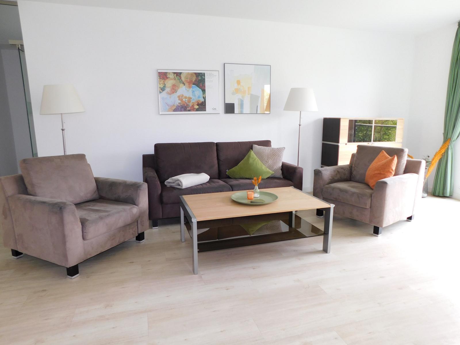 Wohnzimmer mit Sofa, zwei Sesseln, Couchtisch und Wandbildern.