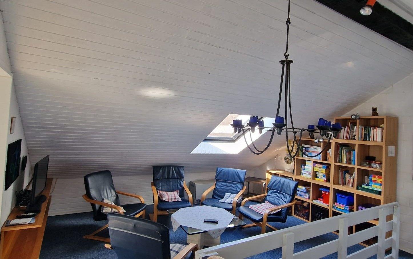 Ein Wohnzimmer mit Sitzgelegenheiten, Bücherregal und Dachfenster.