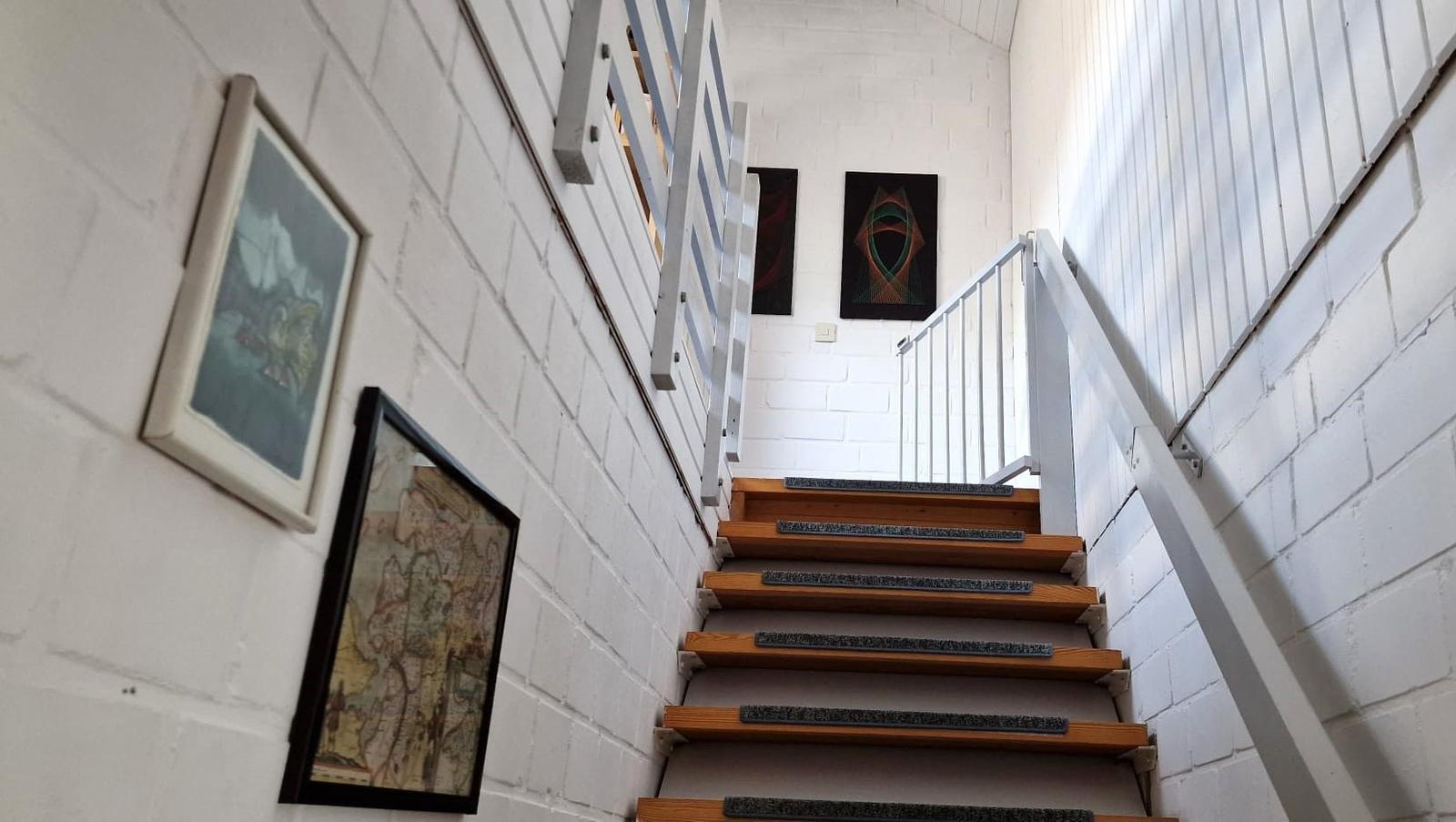 Treppe mit Holzstufen und weißen Wänden, an denen Bilder hängen.