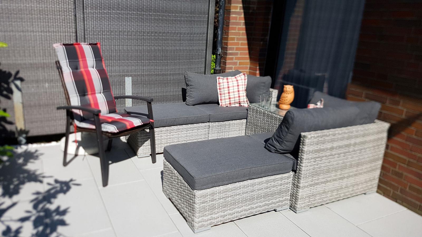 Terrasse mit Sitzgruppe, Liege und Stuhl mit kariertem Kissen.