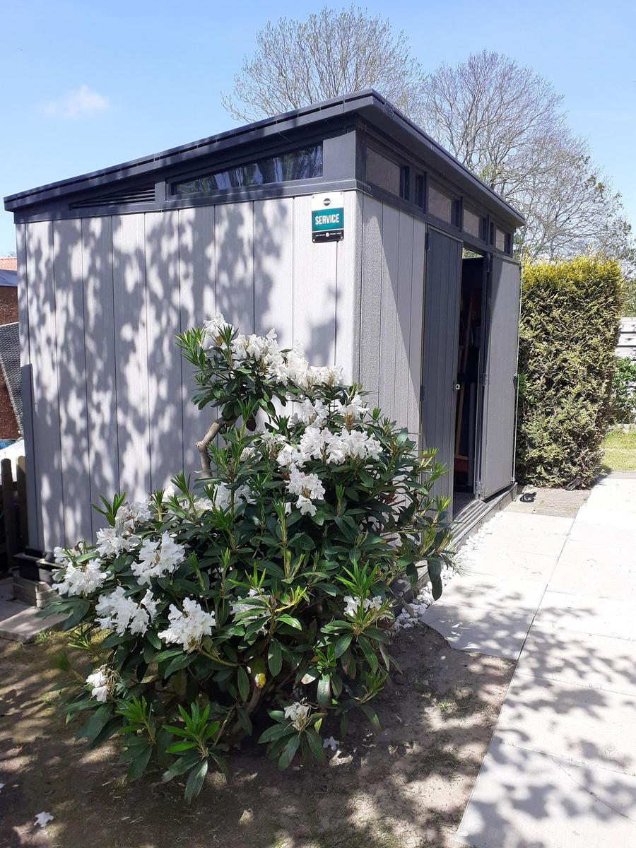 Gärtnerhaus mit blühendem Strauch und gepflastertem Weg.