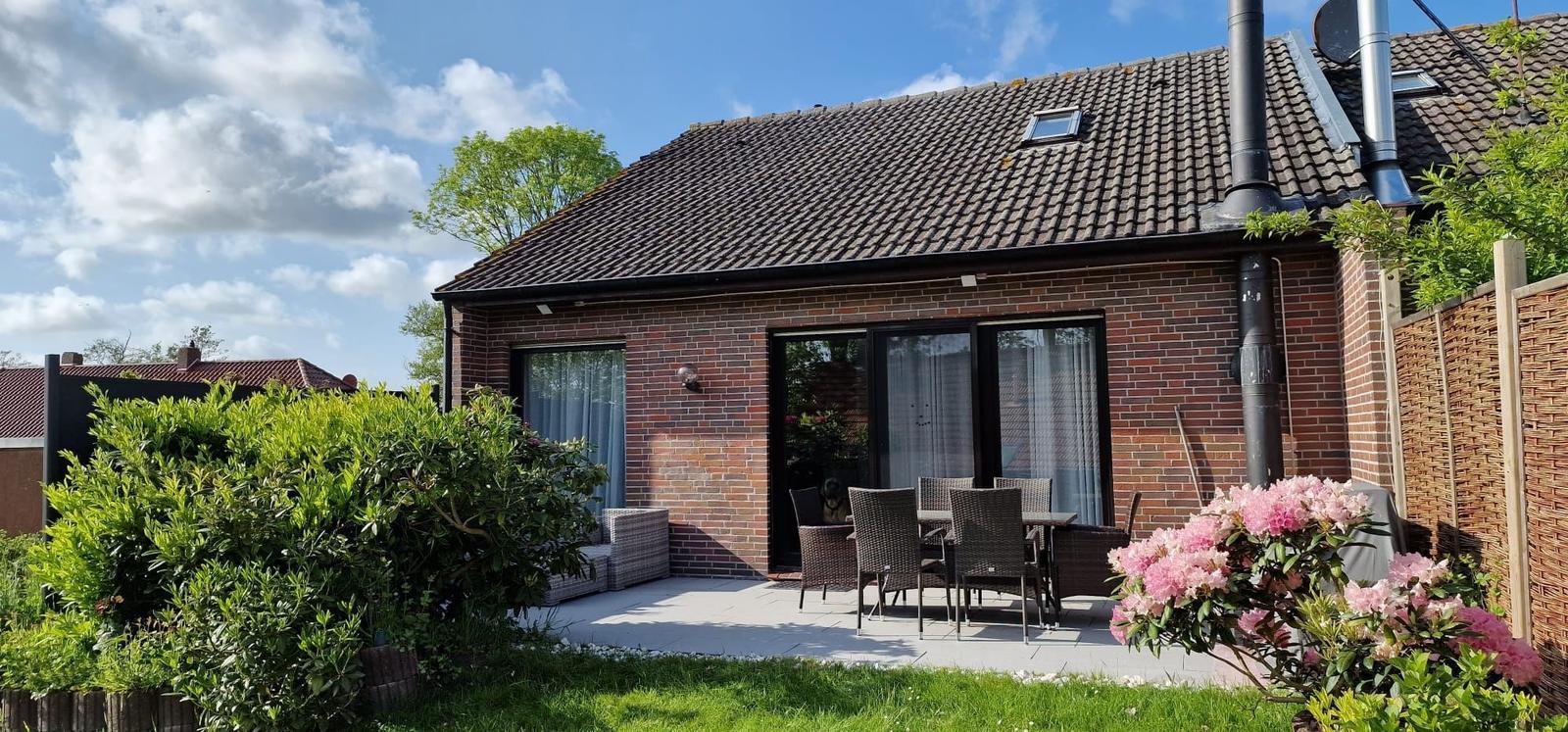 Haus mit Terrasse, Garten und Blumen. Durchgangstür und Fenster sind sichtbar.
