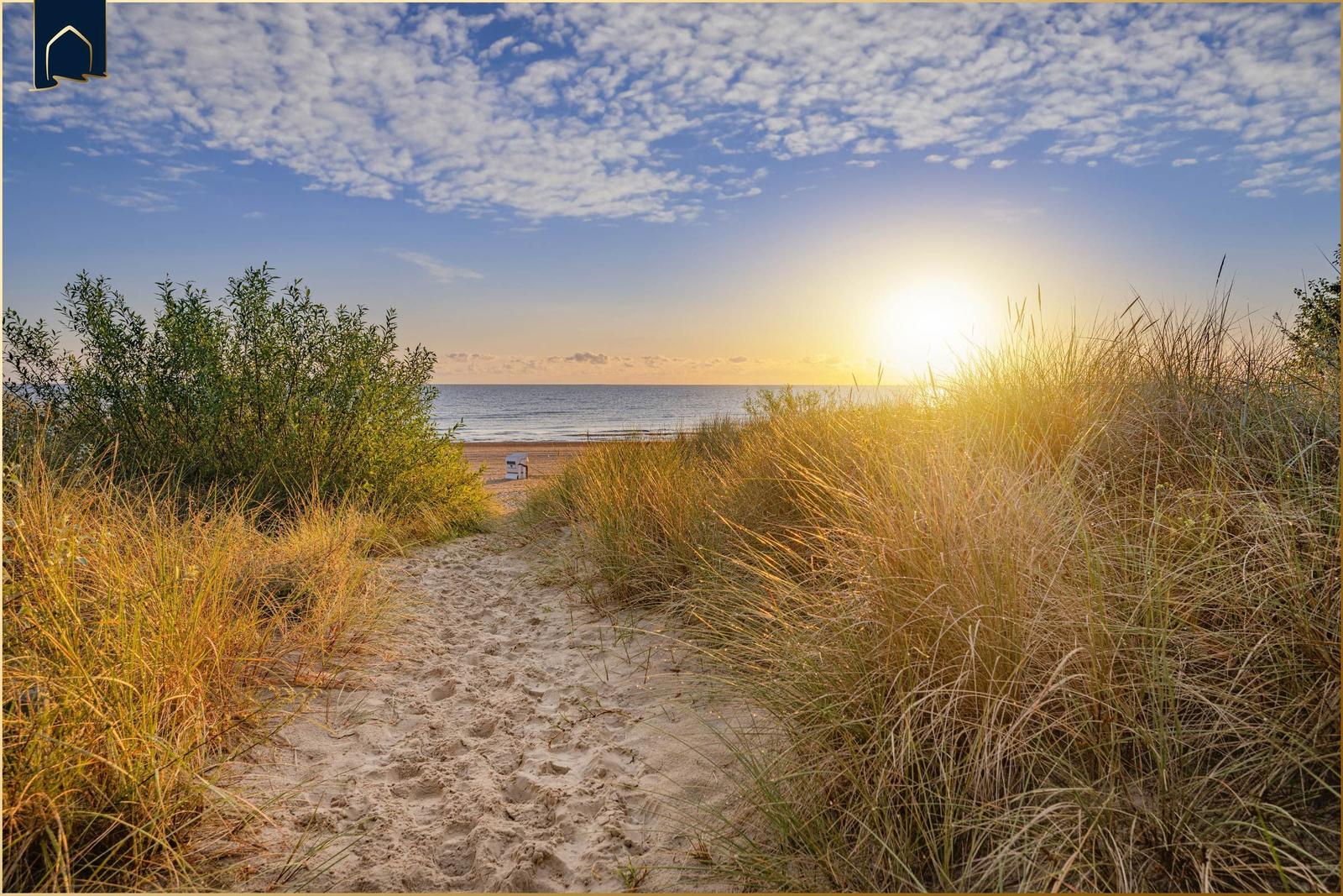 Sandweg führt durch Gras zu Strand und Meer bei Sonnenuntergang.