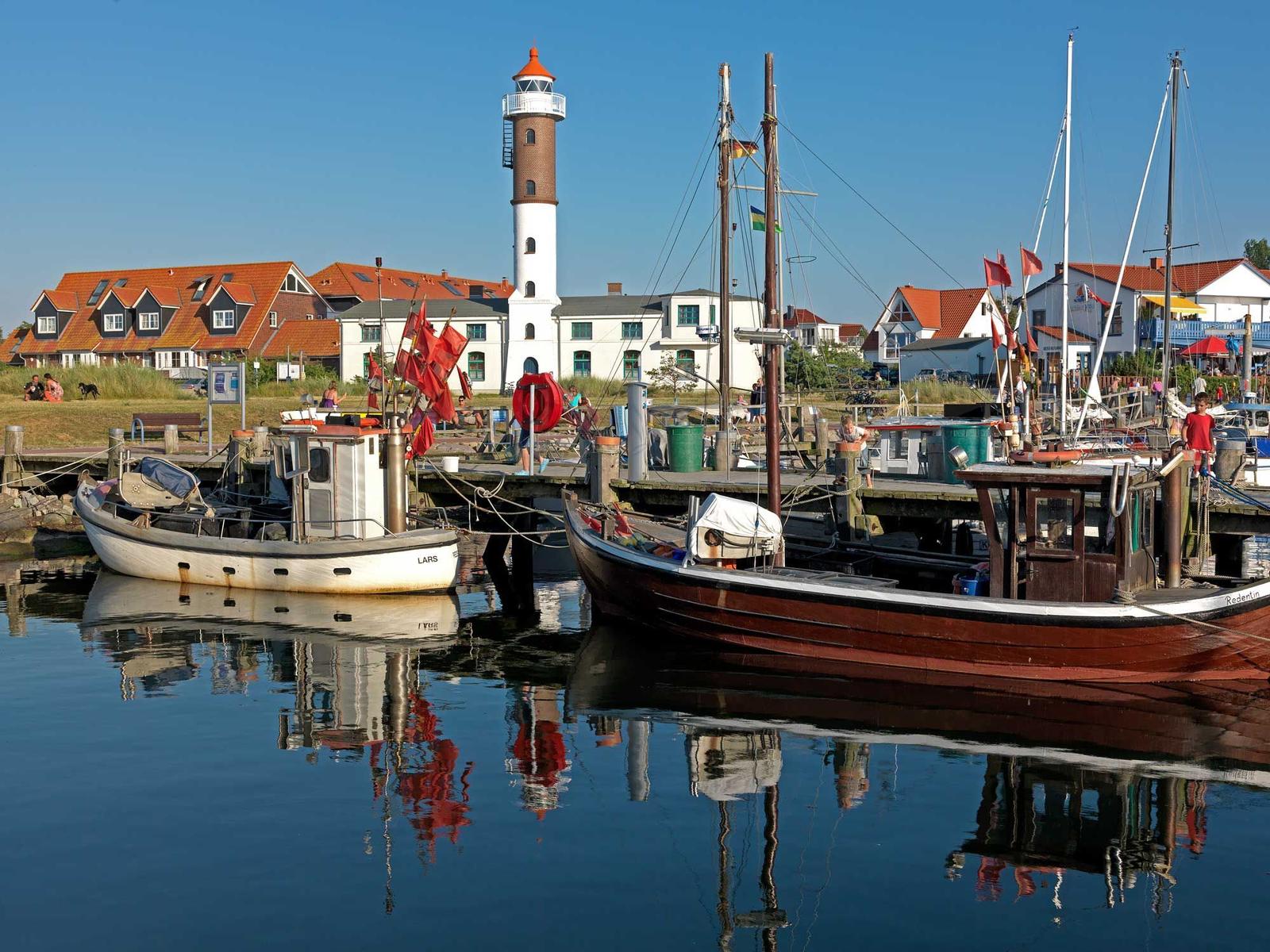 Hafen mit Booten, Leuchtturm und Häusern am Wasser.