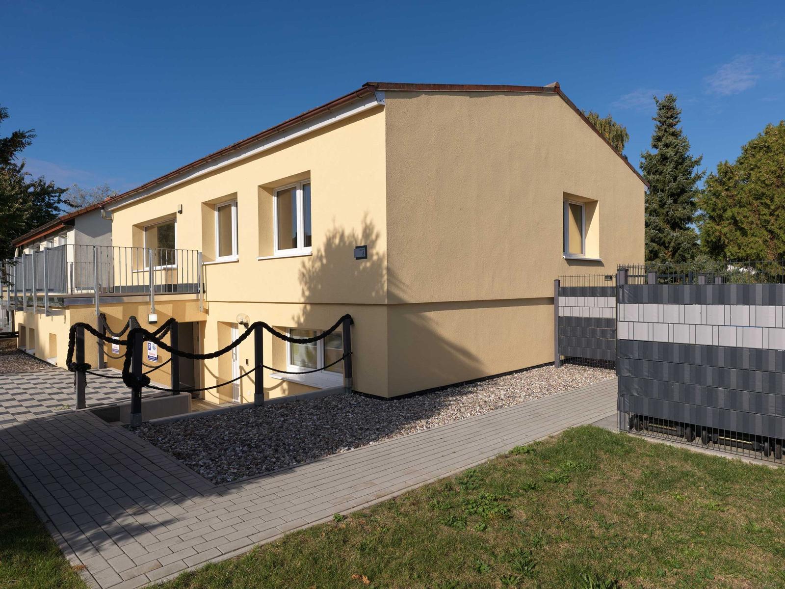 Zweistöckiges Haus mit Balkon, gepflastertem Weg und Grünfläche.