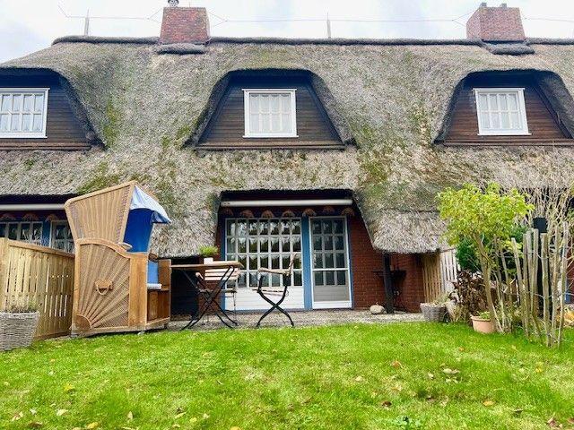Haus mit Strohdach, Garten und Terrasse mit Gartenmöbeln.