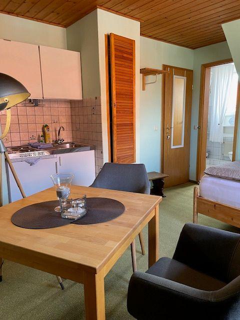 Küche, Essbereich und Schlafzimmer in einer Wohnung mit Holzdecke und grünem Teppichboden.