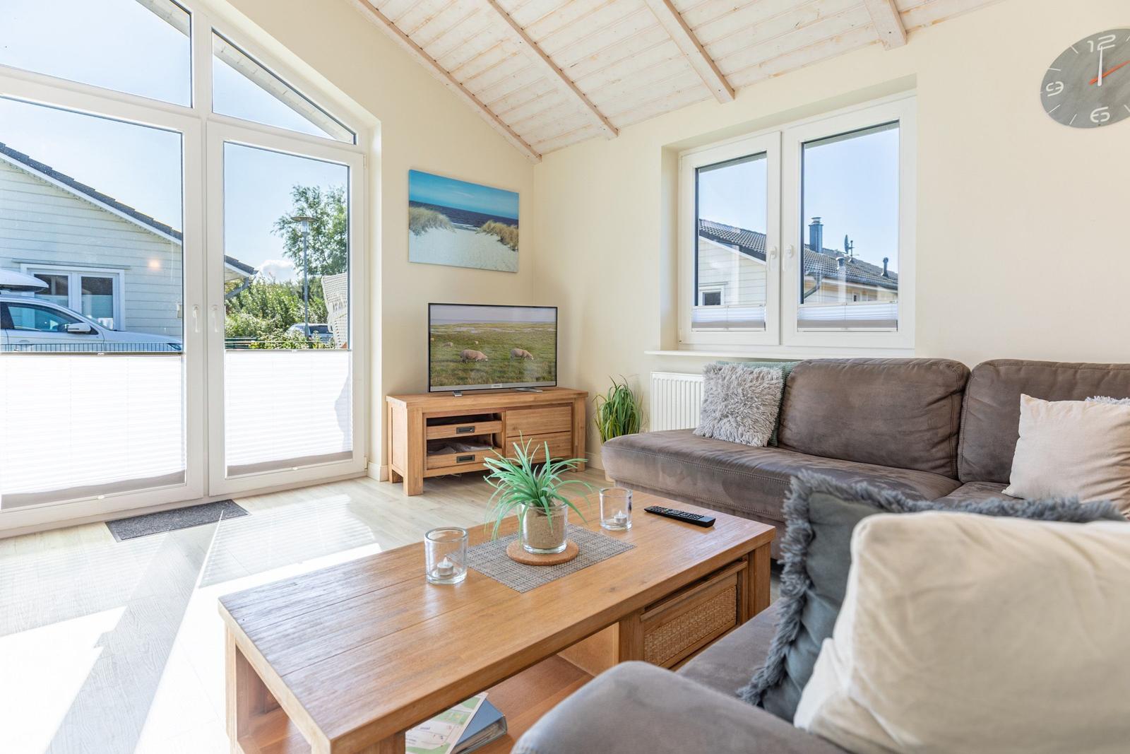 Wohnzimmer mit Sofa, Couchtisch und TV. Große Fenster und Holzdecke.