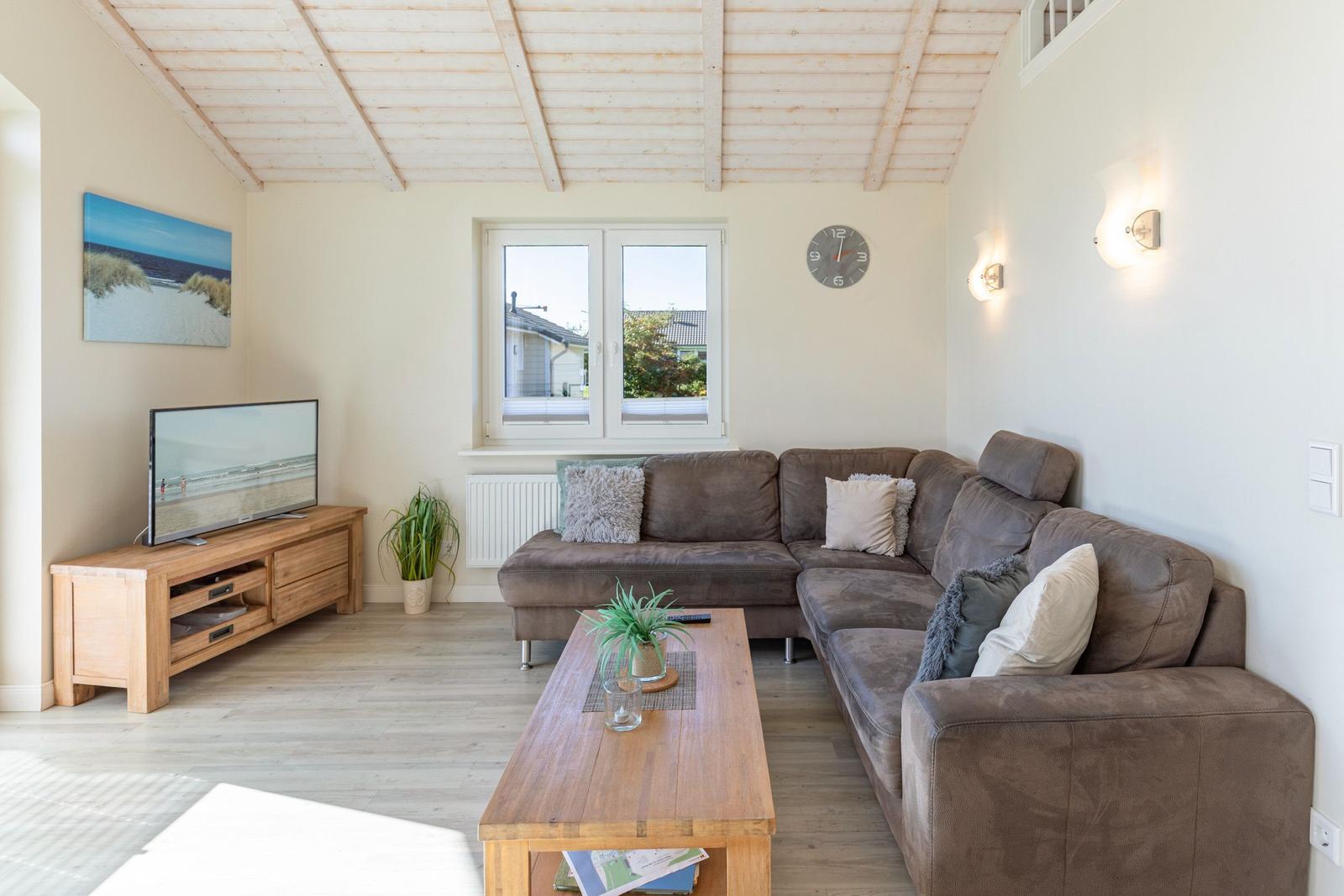 Wohnzimmer mit Sofa, Couchtisch und Fernseher. Holzdecke und Fenster.
