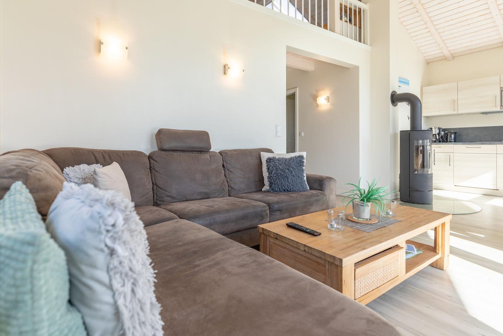 Großer Wohnbereich mit Sofa, Couchtisch und Kaminofen. Küche im Hintergrund.