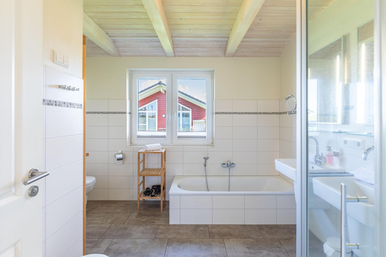 Badezimmer mit Badewanne, Fenster und Dusche. Holzdecke und Fliesen.