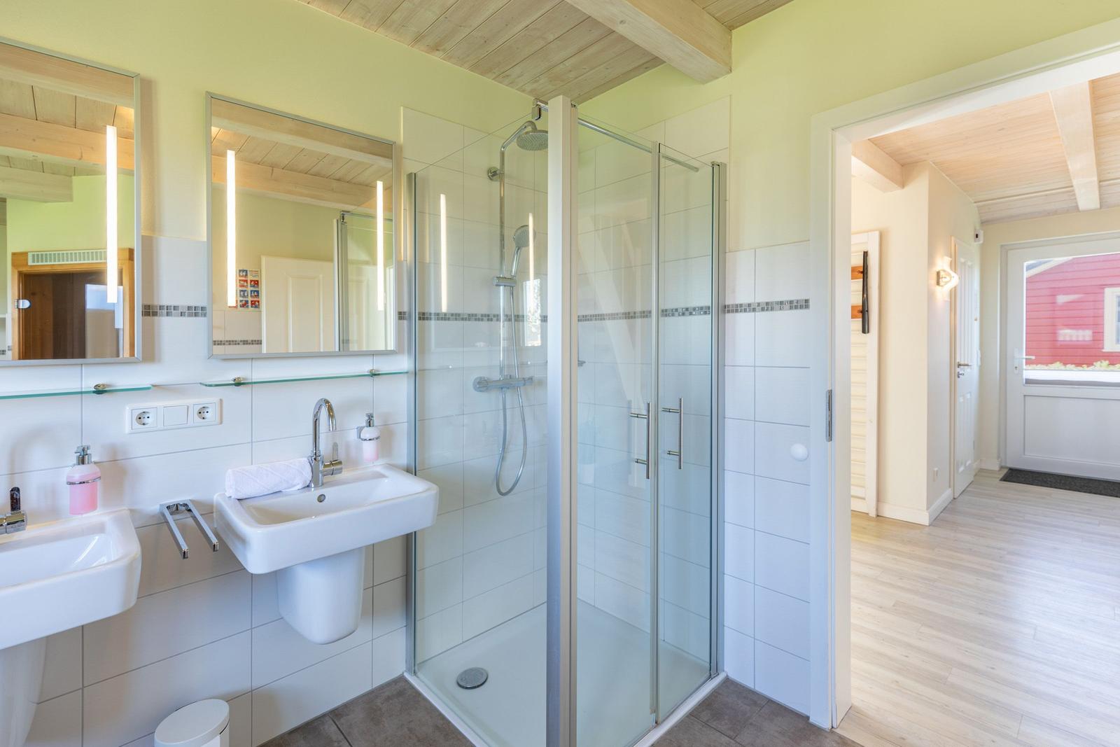 Badezimmer mit Dusche, zwei Waschbecken und Spiegeln mit Beleuchtung.