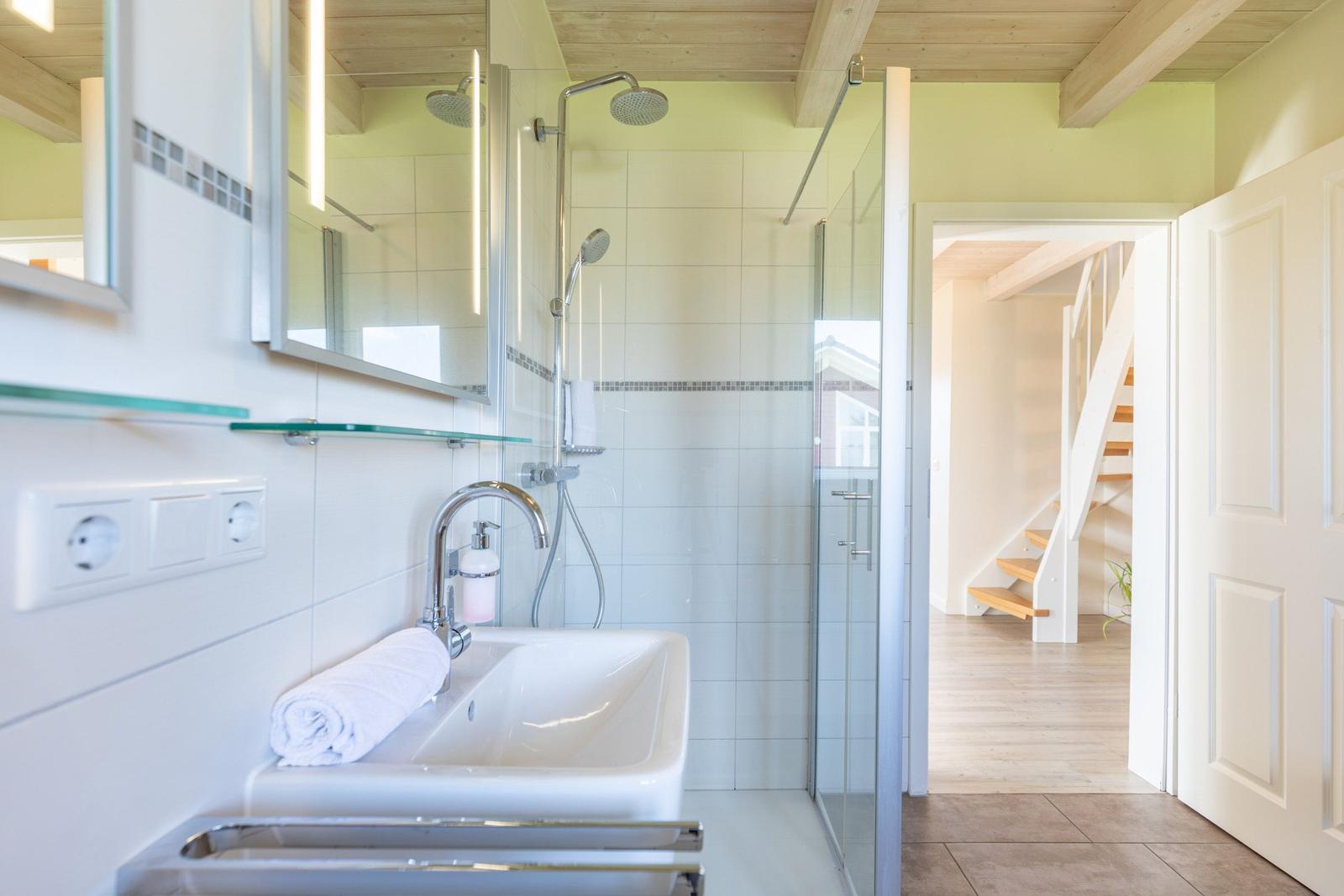 Badezimmer mit Dusche, Waschbecken und Spiegel. Durchgang zur Treppe.