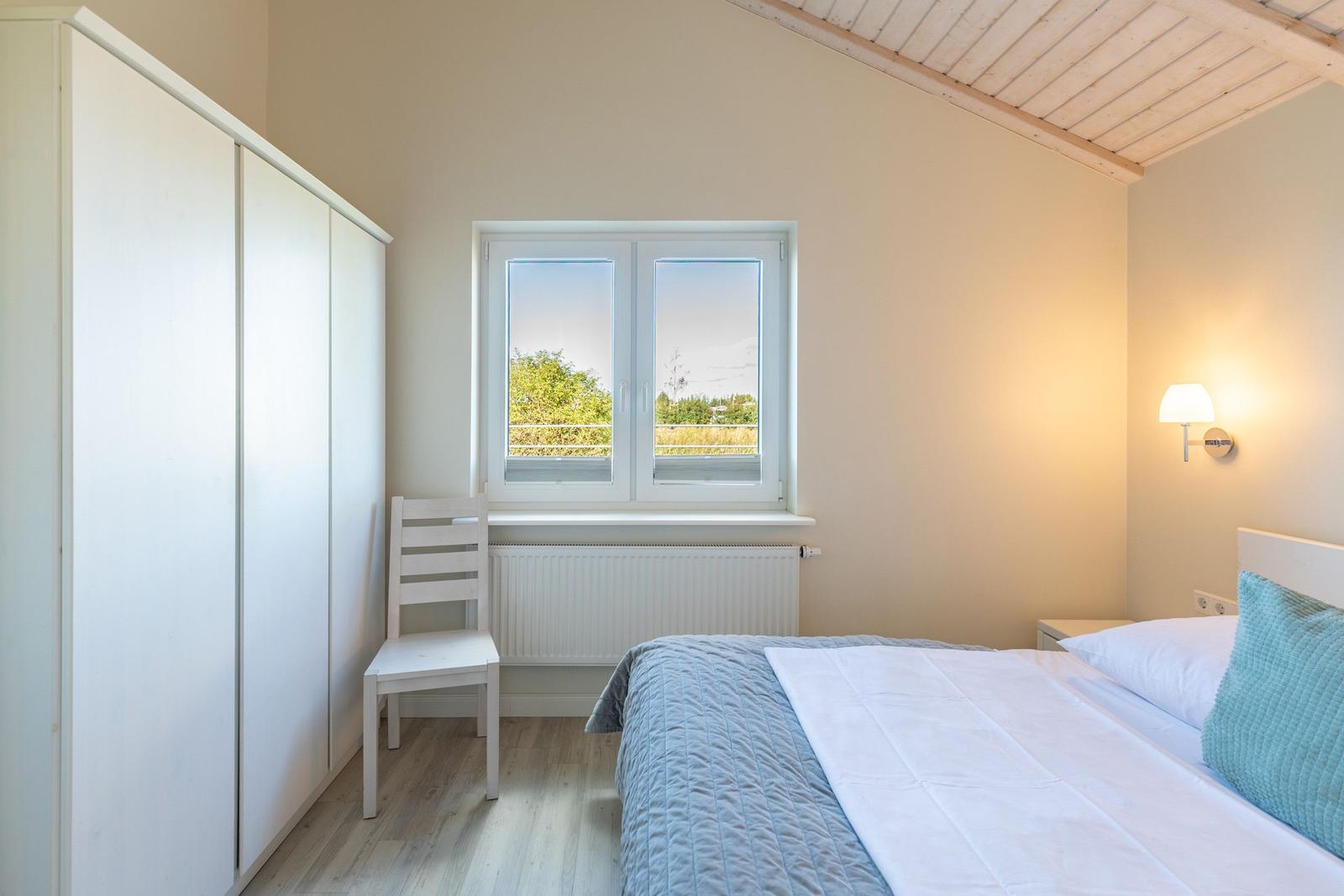 Schlafzimmer mit Bett, Kleiderschrank und Fenster mit Blick auf Grünfläche.