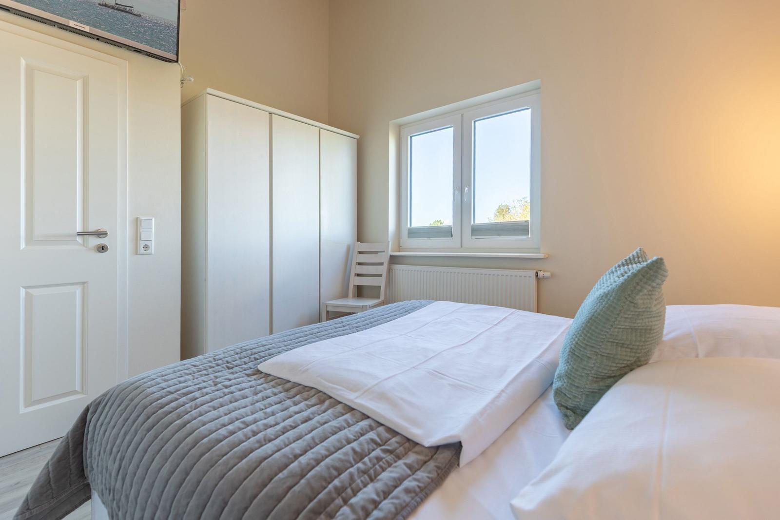 Schlafzimmer mit Bett, Kleiderschrank und Fenster.