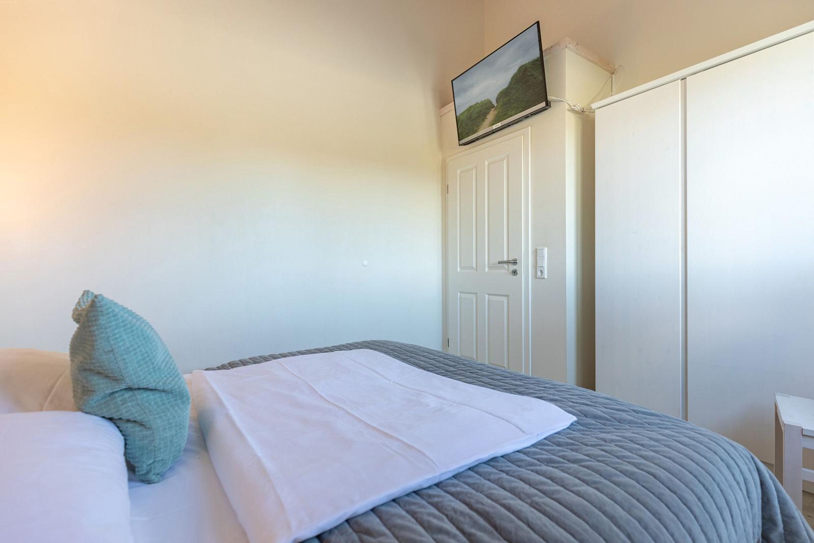 Schlafzimmer mit Bett, Kleiderschrank und Fernseher an der Wand.
