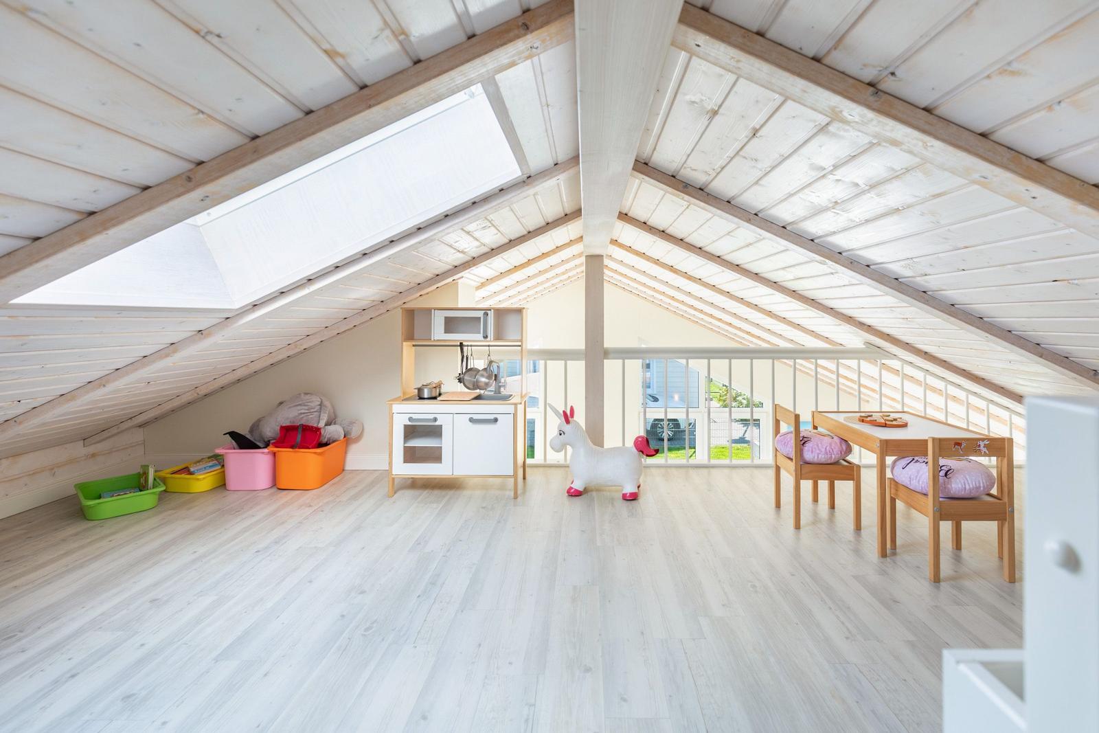 Kinderzimmer mit Spielküche, Tisch, Stühlen und Spielzeug unter Dachschrägen.
