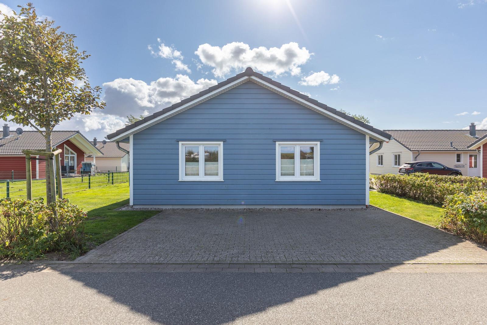 Blau gestrichenes Haus mit weißen Fenstern und gepflastertem Vorplatz.