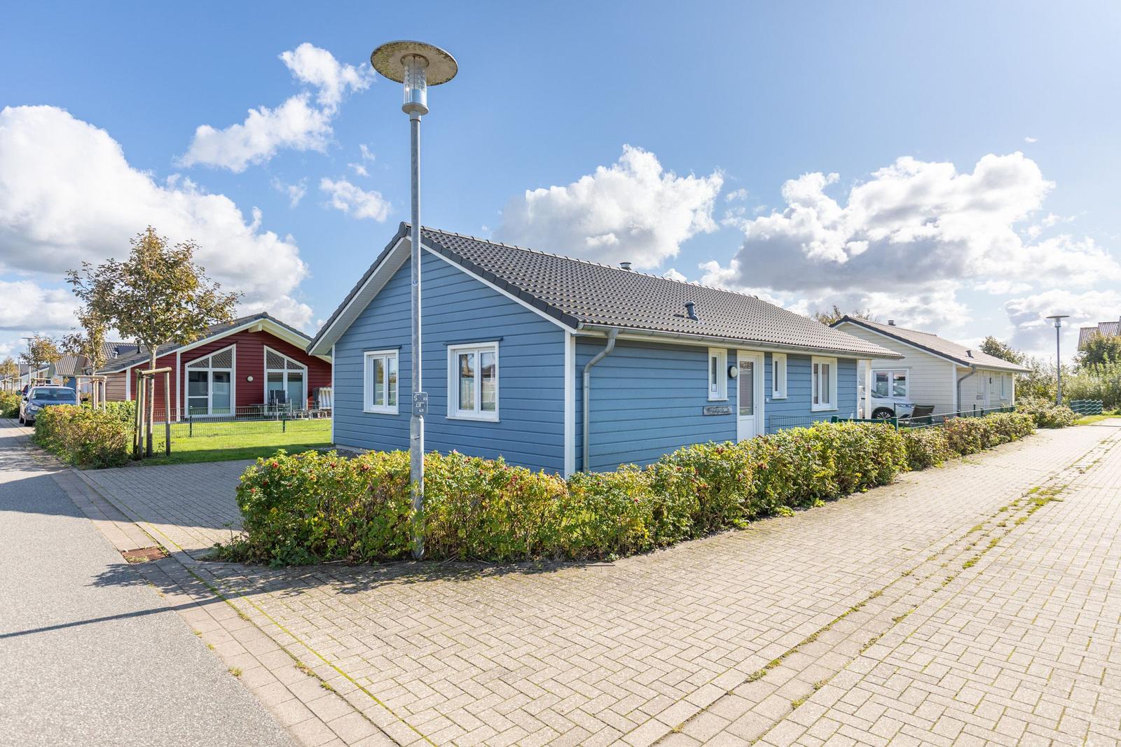 Blau gestrichenes Ferienhaus mit weißem Fensterrahmen und begrüntem Vorgarten.