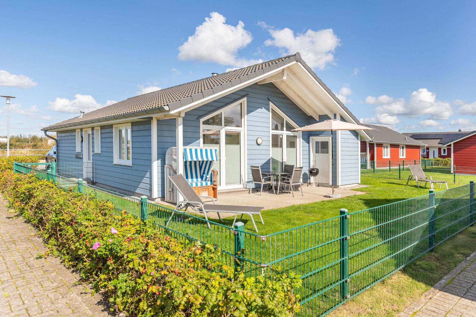 Blau gestrichenes Ferienhaus mit Terrasse, Garten und Sonnenliegen.
