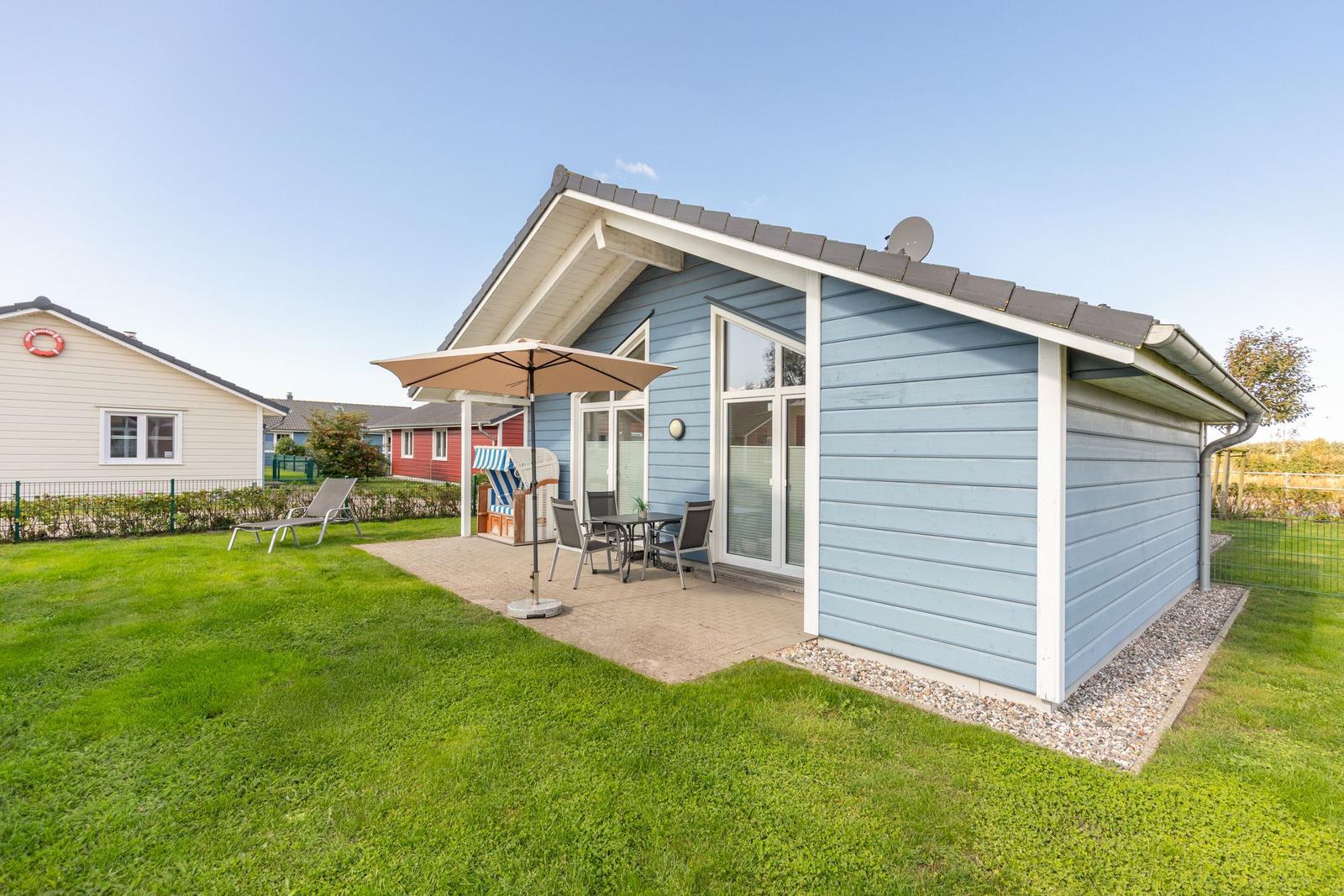 Blau gestrichenes Ferienhaus mit Terrasse, Sonnenschirm und Garten.