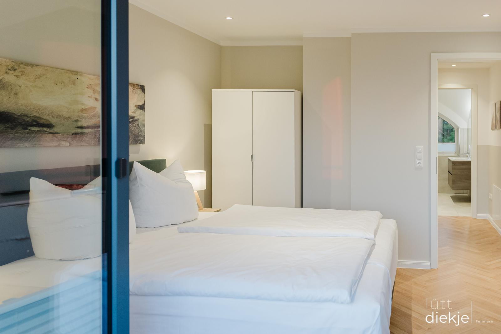 Schlafzimmer mit Doppelbett, Kleiderschrank und Blick in das Badezimmer.