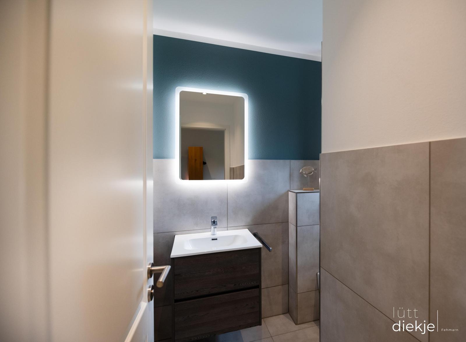 Badezimmer mit beleuchtetem Spiegel und Waschbecken.