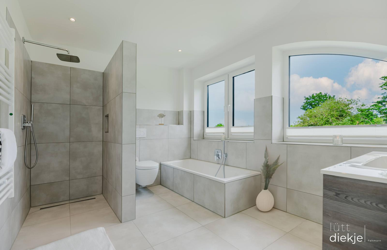 Badezimmer mit Dusche, Badewanne und großem Fenster mit Blick auf Grün.